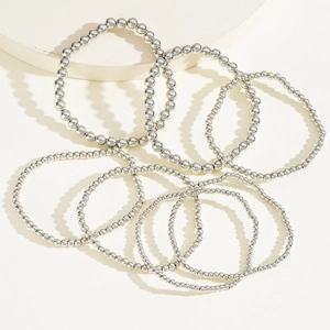 Detailed close-up of a 7-piece set of silver beaded stretch bracelets on a stone display