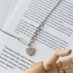 Close-up of silver heart pendant and chunky paperclip chain on artistic book background
