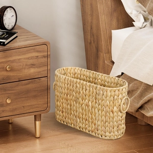 Narrow woven seagrass storage basket with ring handles placed in a bedroom setting