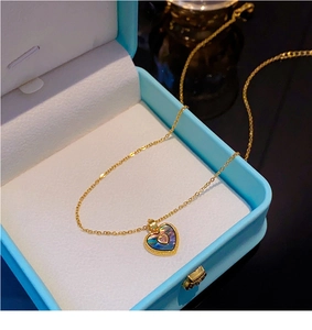 Collier cœur doré avec incrustation en nacre et gemme rose dans un écrin de bijoux bleu clair