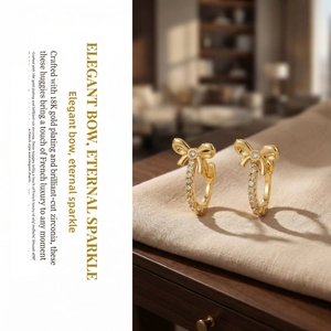 Detailed view of 18K gold plated bow huggie earrings with cubic zirconia on linen