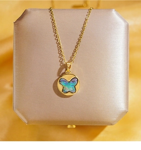 Détail du collier doré avec pendentif papillon en nacre irisante sur boîte à bijoux brossée