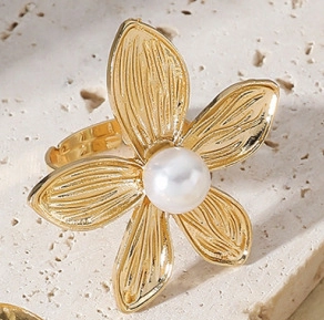Macro shot of gold flower ring with center pearl and radial brushed texture petals