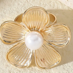 Elegant gold metal flower ring with white pearl center on a textured stone surface