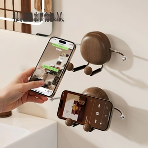 Wall-mounted walnut wood phone holder with silver metal arm shown in bathroom setting