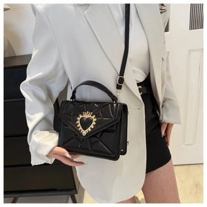 Close-up of black quilted shoulder bag with gold heart clasp on a model in a modern room