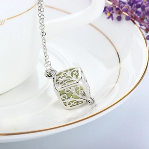 Close-up of hollow cube necklace pendant with glowing green bead on white coffee cup