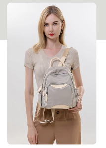 Detailed view of light gray nylon backpack with beige handles and multi-layer zippers