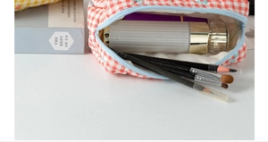 Top view of quilted orange plaid cosmetic bag with brushes and skincare bottles