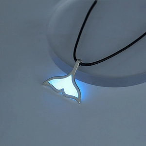 Detailed view of a whale tail pendant with bright blue glow in the dark effect on black cord