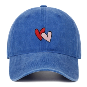 Detailed view of red and pink embroidered heart on blue washed denim baseball cap