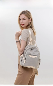 Detailed view of light gray nylon backpack with beige leather trim worn by model