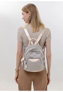 Detail view of a compact grey-purple nylon backpack with elegant beige leather trim details