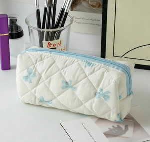 Détail de la trousse de maquillage matelassée blanche avec nœuds bleus et zip