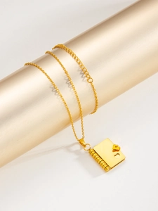 Macro detail of gold book pendant with heart and O-chain on elegant cylinder stand