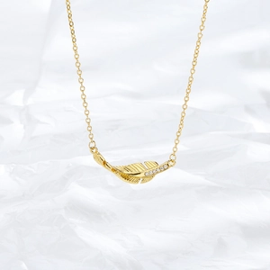 Close-up of golden feather necklace with micro-pave white zircon stones on silk background