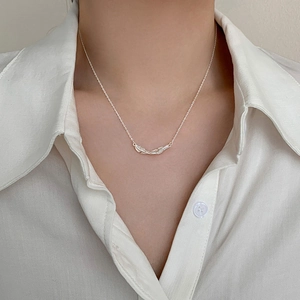 Detailed view of silver feather pendant necklace worn by model on white shirt