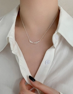 Detailed view of silver feather pendant necklace worn with a white button-down shirt