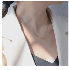 Detailed close-up of a minimalist gold bead pendant on a slender snake chain necklace