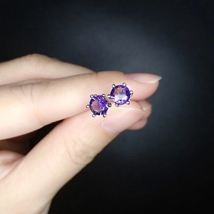 Close-up of hand holding purple zircon earrings with classic six-prong silver setting