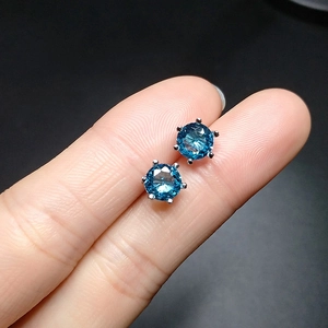 Macro shot of blue sapphire stud earrings in six-prong silver setting on fingers