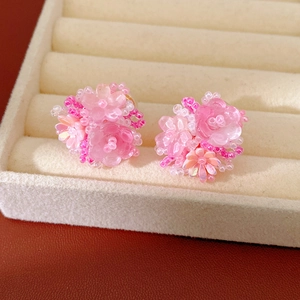 Close-up of handmade pink resin flower beaded earrings displayed on a beige jewelry tray