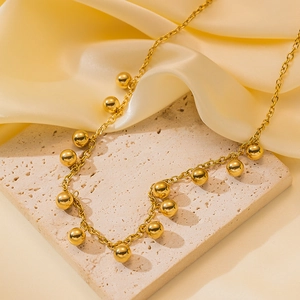 Minimalist titanium steel necklace with polished gold beads on beige stone background
