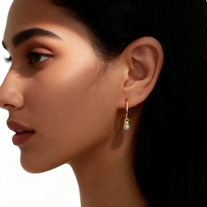 Close-up of elegant gold hoop earrings with white pearl pendants on a female model