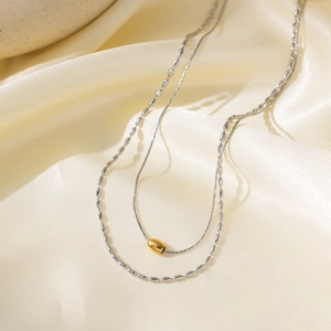 Double layer minimalist necklace with gold cylinder pendant on luxury silk background