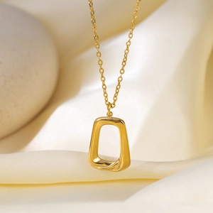 Golden geometric twisted trapezoid hollow pendant necklace on elegant cream fabric