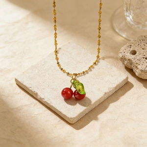 Elegant gold chain necklace with red cherry pendants and a green leaf on a stone pedestal