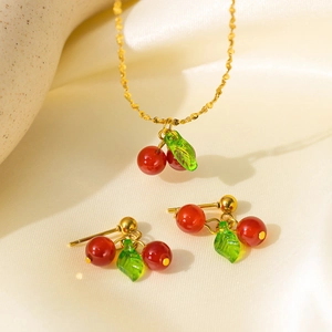 Close-up of cherry pendant necklace and earrings set on a beige textured stone block