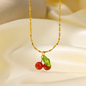 Close-up of cherry pendant necklace with red agate beads and green leaf on gold chain