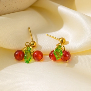 Close-up of cherry drop earrings with red garnet beads and green glass leaves on silk