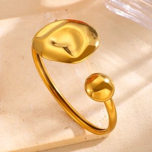 Macro detail of asymmetric gold stainless steel cuff bracelet featuring shell and ball ends