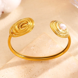 Detail view of an asymmetric gold cuff bracelet with spiral design and pearl accent