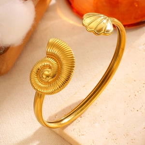 Close-up of gold stainless steel bangle with asymmetrical conch and shell design