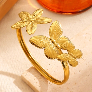 Detailed macro shot of golden stainless steel bracelet with flower and butterfly motifs.