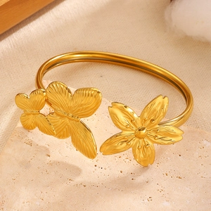 Close-up detail of golden stainless steel bangle with butterfly and flower charms