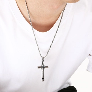 Detalle de un colgante de silbato de cruz gótica de acero inoxidable en camiseta blanca