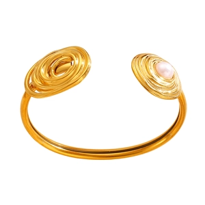 Detailed view of gold asymmetric cuff bracelet with concentric swirls and pearl accent
