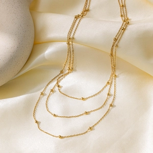 Three-layer gold beaded chain choker necklace on elegant cream silk background