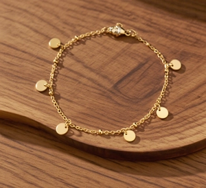 Detailed shot of gold titanium steel anklet with six shiny circular sequins on wood surface