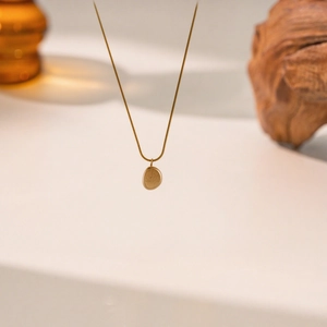 Minimalistische goldene Schlangenkette mit ovalem Gravuranhänger auf neutralem Grund