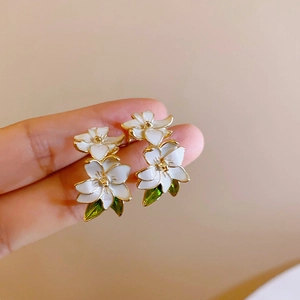 Nahaufnahme eleganter weißer Blumenohrringe mit grünen Blättern und Goldfinish