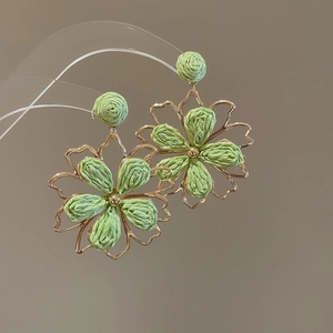 Detailansicht von grün geflochtenen Blumenohrringen mit goldfarbenem Rahmen.