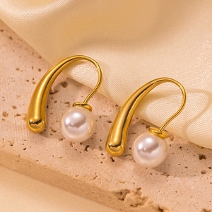 Elegant gold drop earrings with white pearls on a textured stone and silk background
