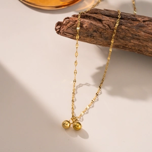 Minimalist gold ball titanium steel necklace set displayed on natural wood with warm lighting