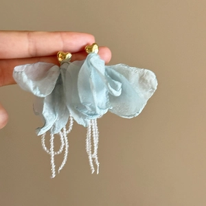 Close-up of blue fabric flower earrings with gold heart studs and bead tassels.