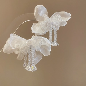 Close-up of elegant white fabric bow earrings with clear beaded tassels and silver pins.